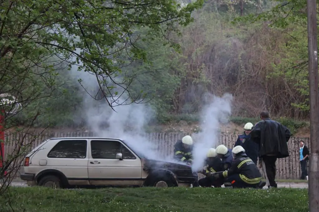 a car with newly burnt front being check by a group of firemen