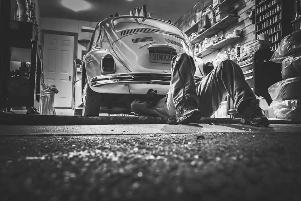 Man under the Volkswagen Beetle car to fix it