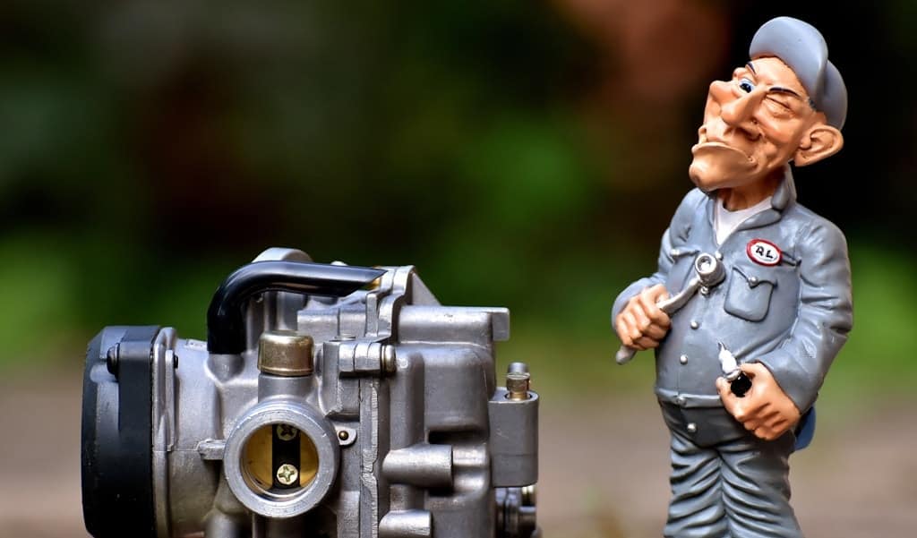 a toy depicting an old auto mechanic holding tools while standing next to a toy car engine