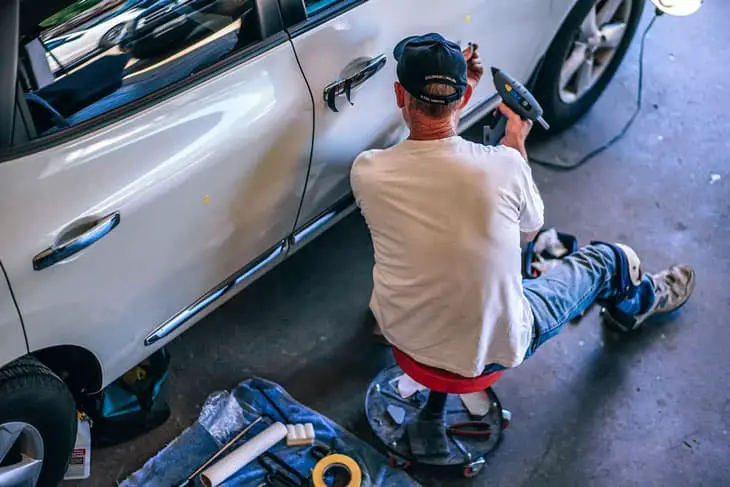 the man is fixing the car door using some car tools